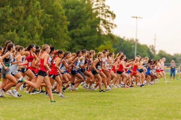 Cross-country runners leaving a grassy start line